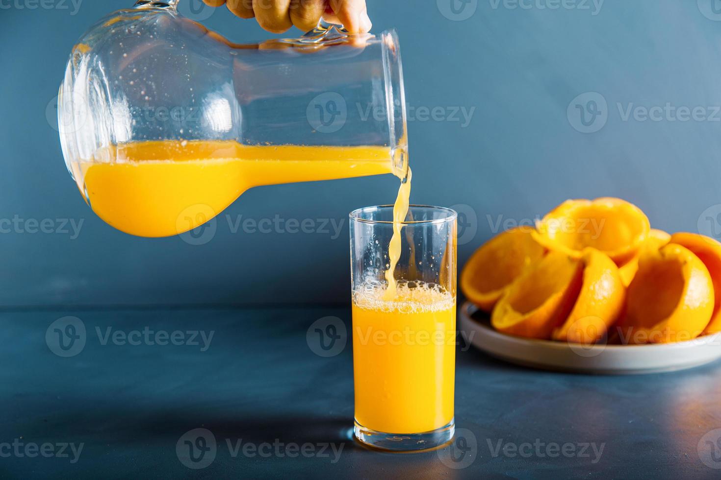 une main anonyme remplit du jus d'orange frais au verre photo