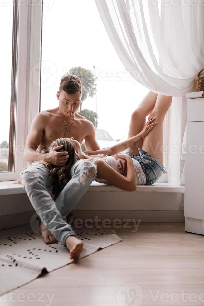 jeune couple assis sur le lit dans un salon et s'amuser ensemble. il la fait toujours rire. jeunes enjoués souriant et s'amusant tout en passant du temps libre à la maison photo