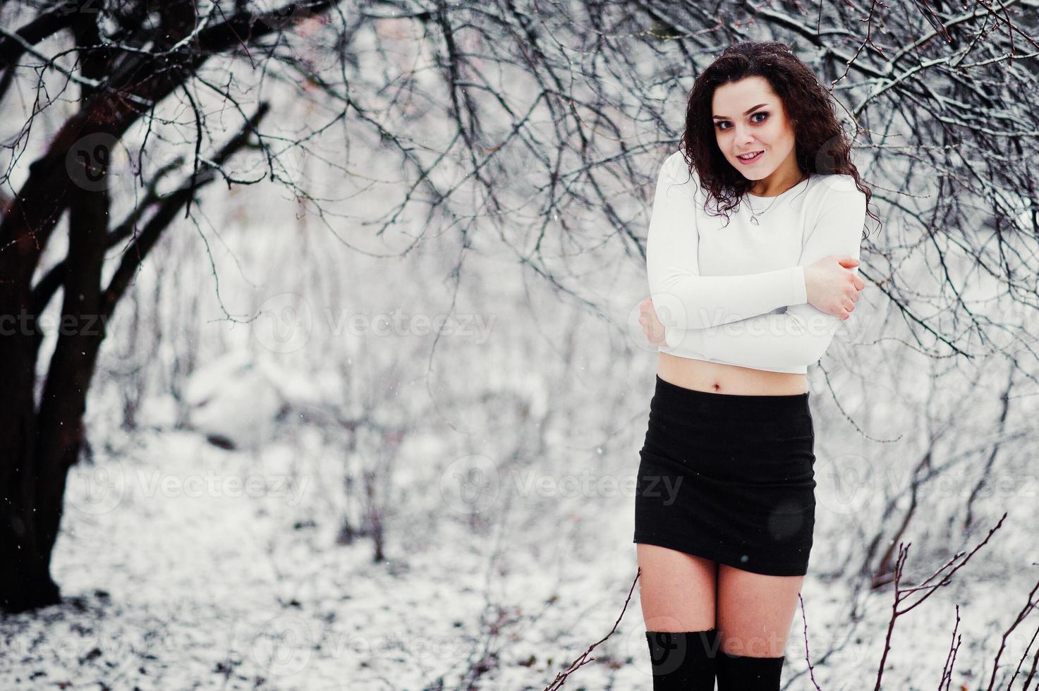 fond de fille brune bouclée chute de neige, usure sur mini jupe noire et bas de laine. modèle sur l'hiver. portrait de mode par temps neigeux. photo tonique instagram.