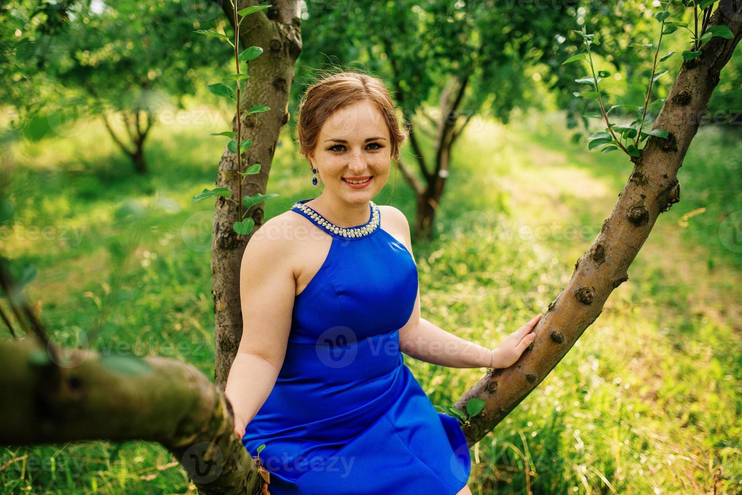 jeune fille en surpoids à la robe bleue posée fond jardin de printemps assis sur l'arbre. photo