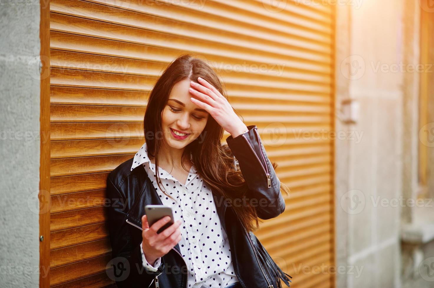 portrait d'une jeune fille élégante portant une veste en cuir avec un téléphone portable à la main texture d'obturation d'arrière-plan. style de modèle de mode de rue. photo