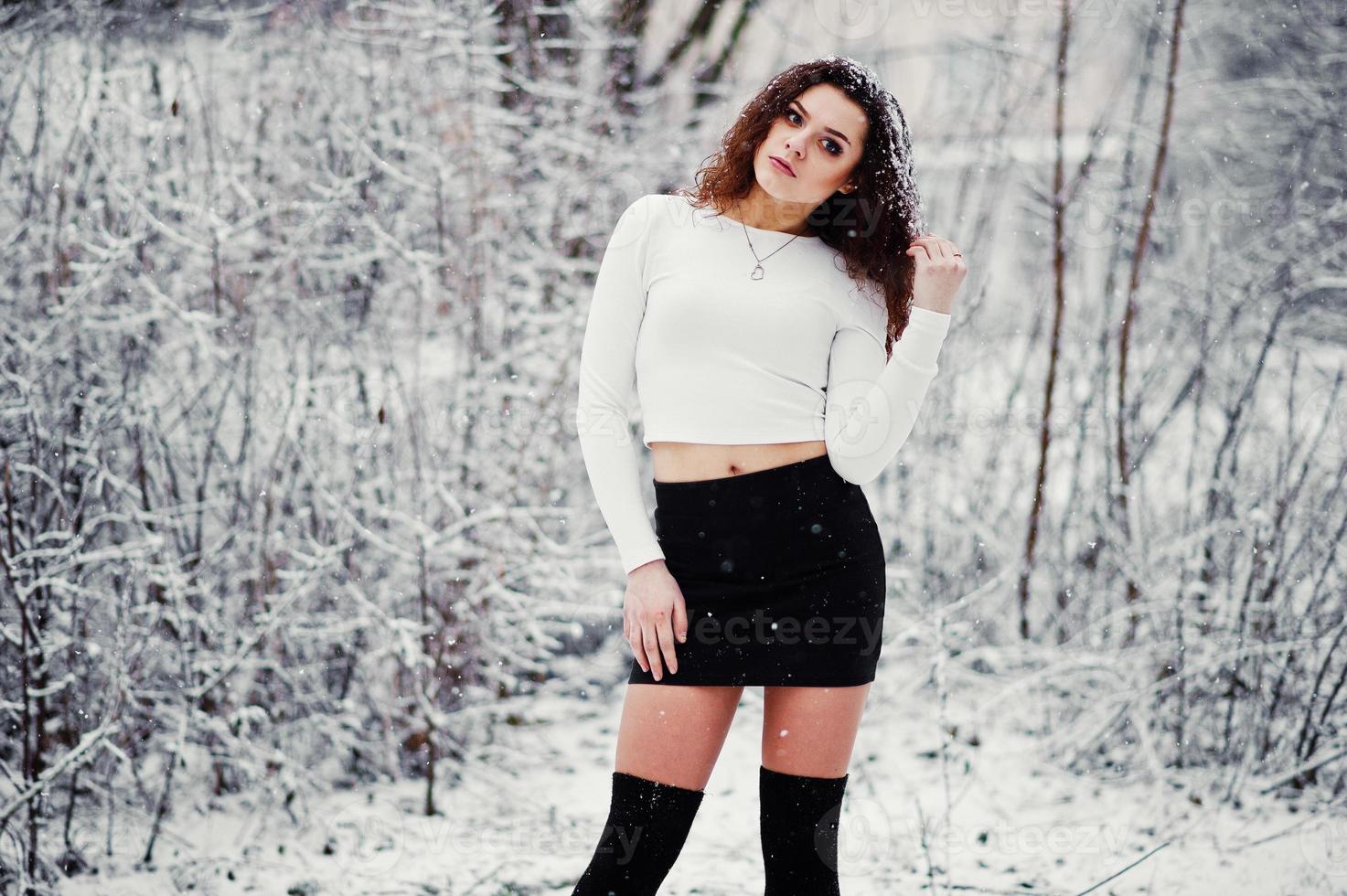 fond de fille brune bouclée chute de neige, usure sur mini jupe noire et bas de laine. modèle sur l'hiver. portrait de mode par temps neigeux. photo tonique instagram.