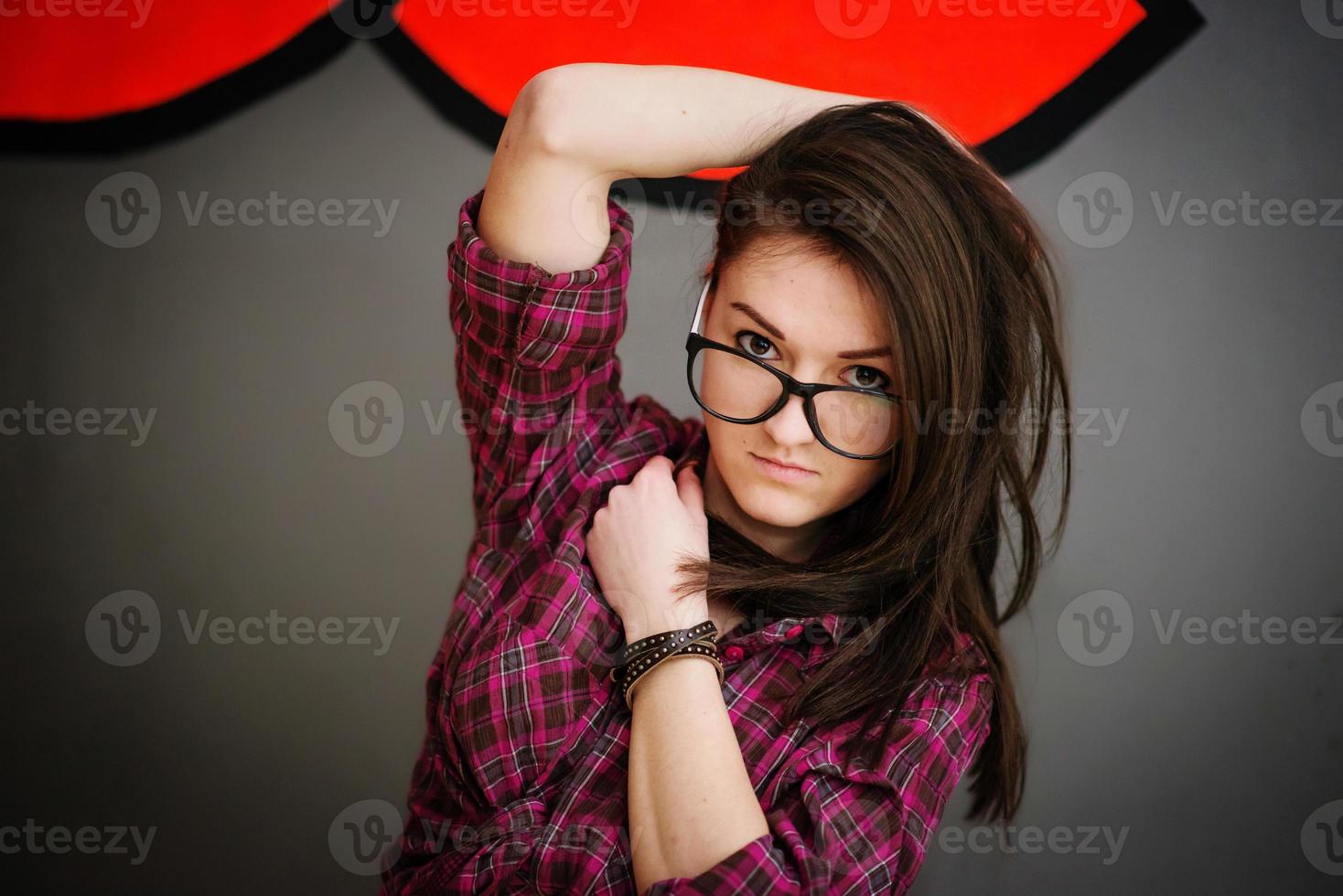 portrait de jeune fille brune sur des lunettes portant des vêtements décontractés fond mur gris avec quelques graffitis. photo