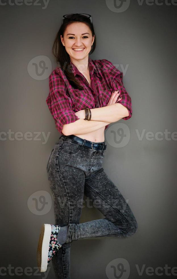 portrait vertical de jeune fille brune avec des lunettes portant des vêtements décontractés fond mur gris. photo