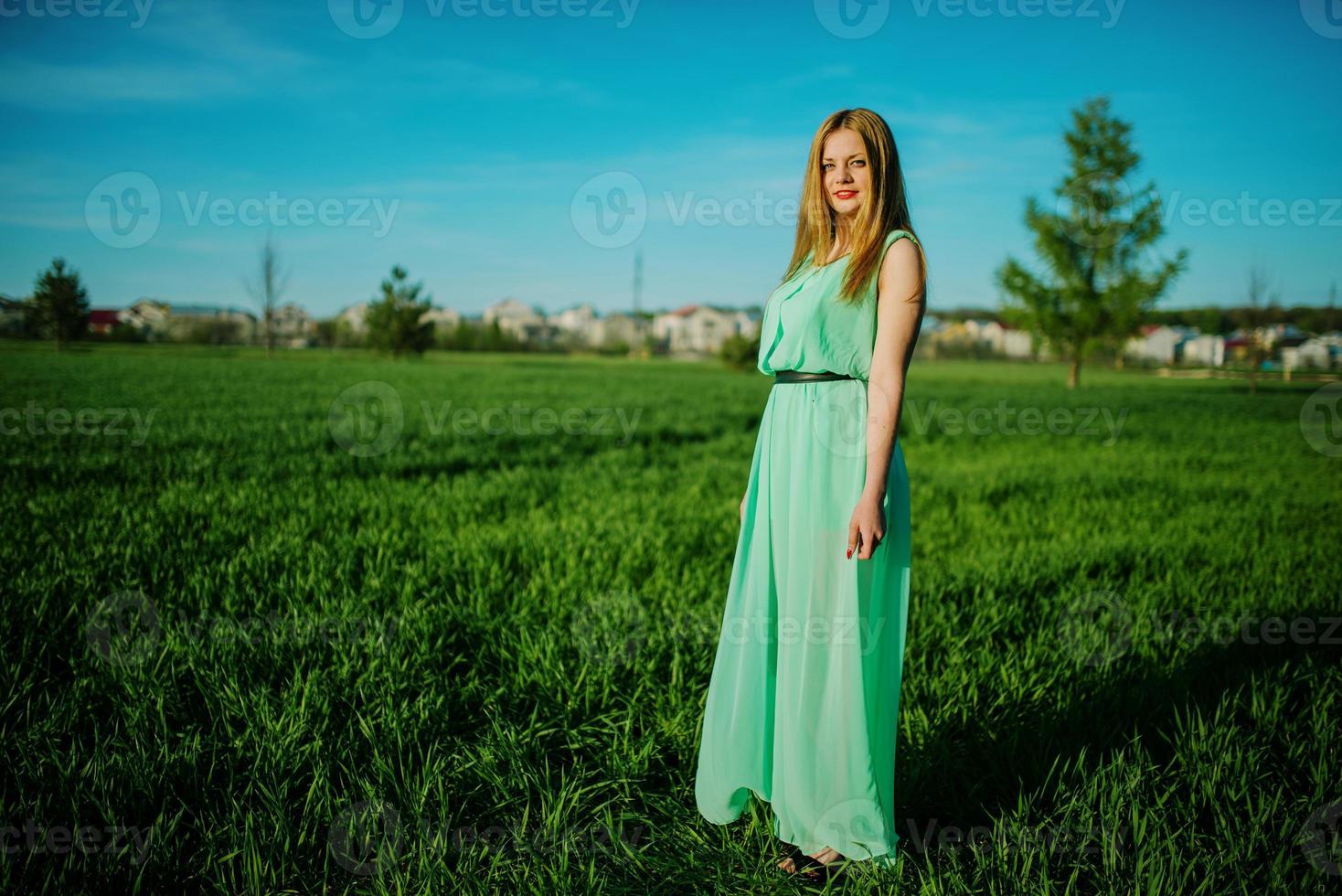 femme dans une belle robe longue turquoise posant sur un pré sur l'herbe. photo