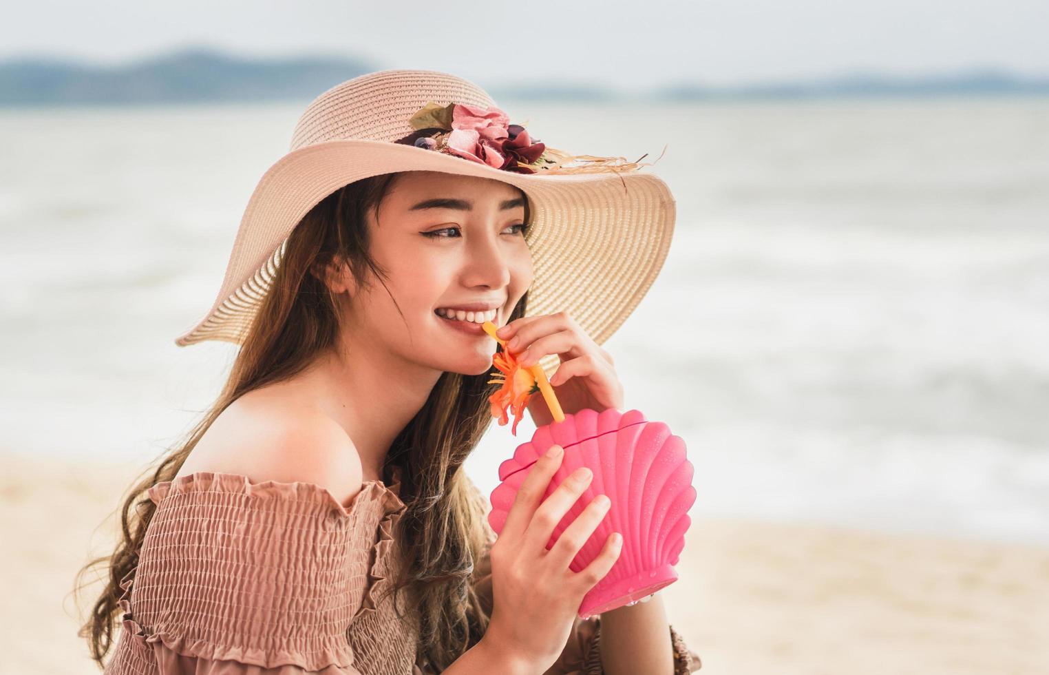 elle boit un cocktail rafraîchissant avec un visage souriant à la plage photo