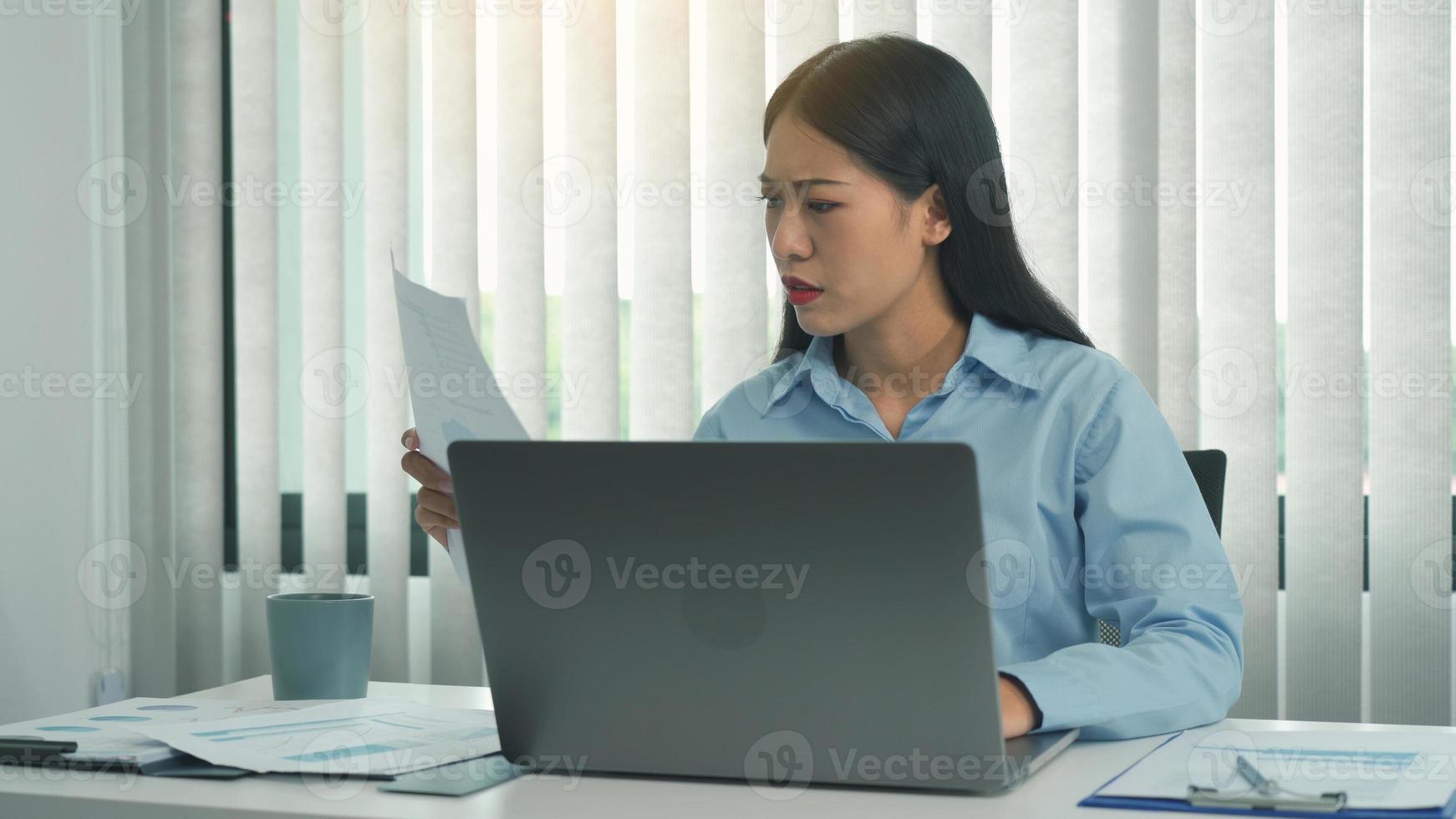 les jeunes femmes asiatiques sont frustrées par les documents lorsqu'elles utilisent l'ordinateur portable à leur bureau. photo