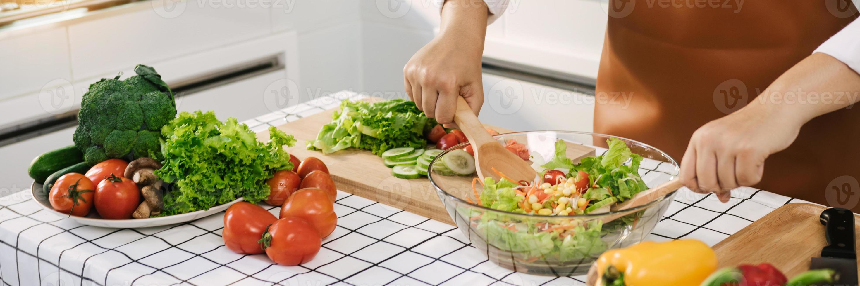 une femme asiatique mélange les ingrédients dans un saladier à la table de cuisson de la cuisine. photo