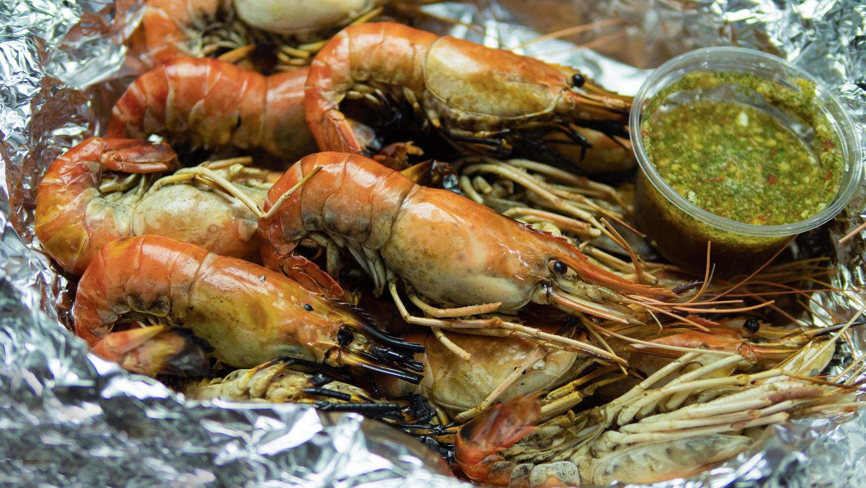 crevettes grillées avec sauce aux fruits de mer contenues dans un emballage alimentaire en papier d'aluminium et un récipient alimentaire en mousse. sauce aux fruits de mer à la thaïlandaise, goût épicé et aigre, ingrédient principal, jus de citron vert, piment frais, sauce de poisson photo