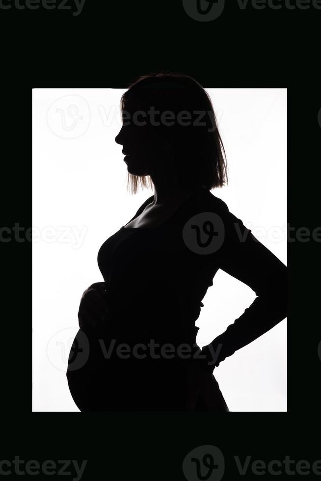 élégante belle femme enceinte dans une robe noire tient ses mains sur son ventre. photo