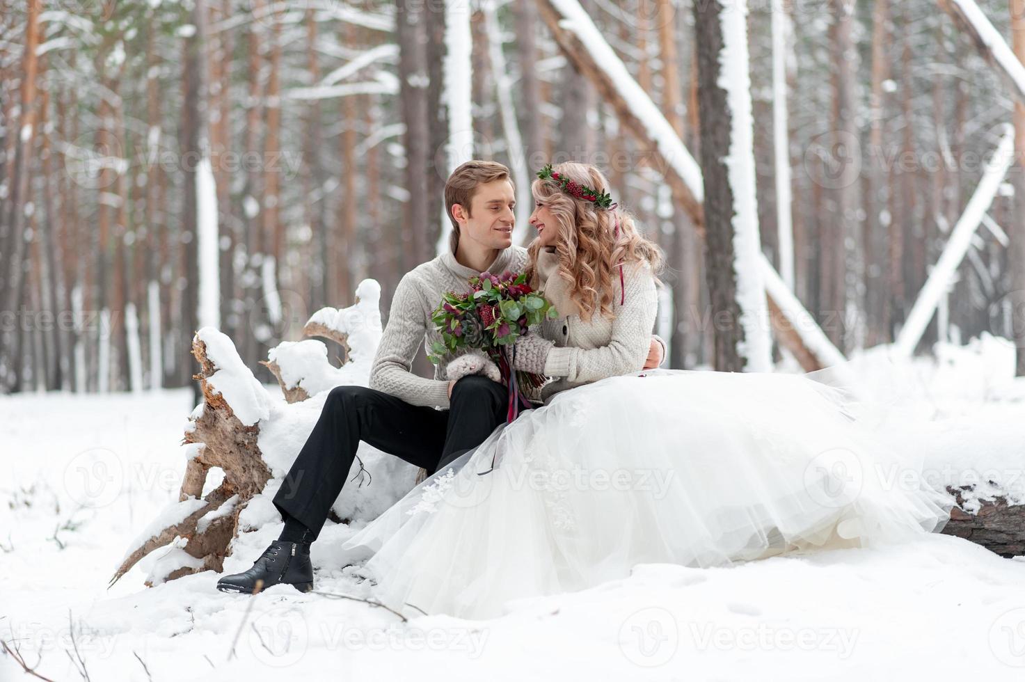 un joli couple amoureux d'un bouquet est assis sur la bûche sur fond de forêt d'hiver. ouvrages d'art. mariage d'hiver. copie espace photo