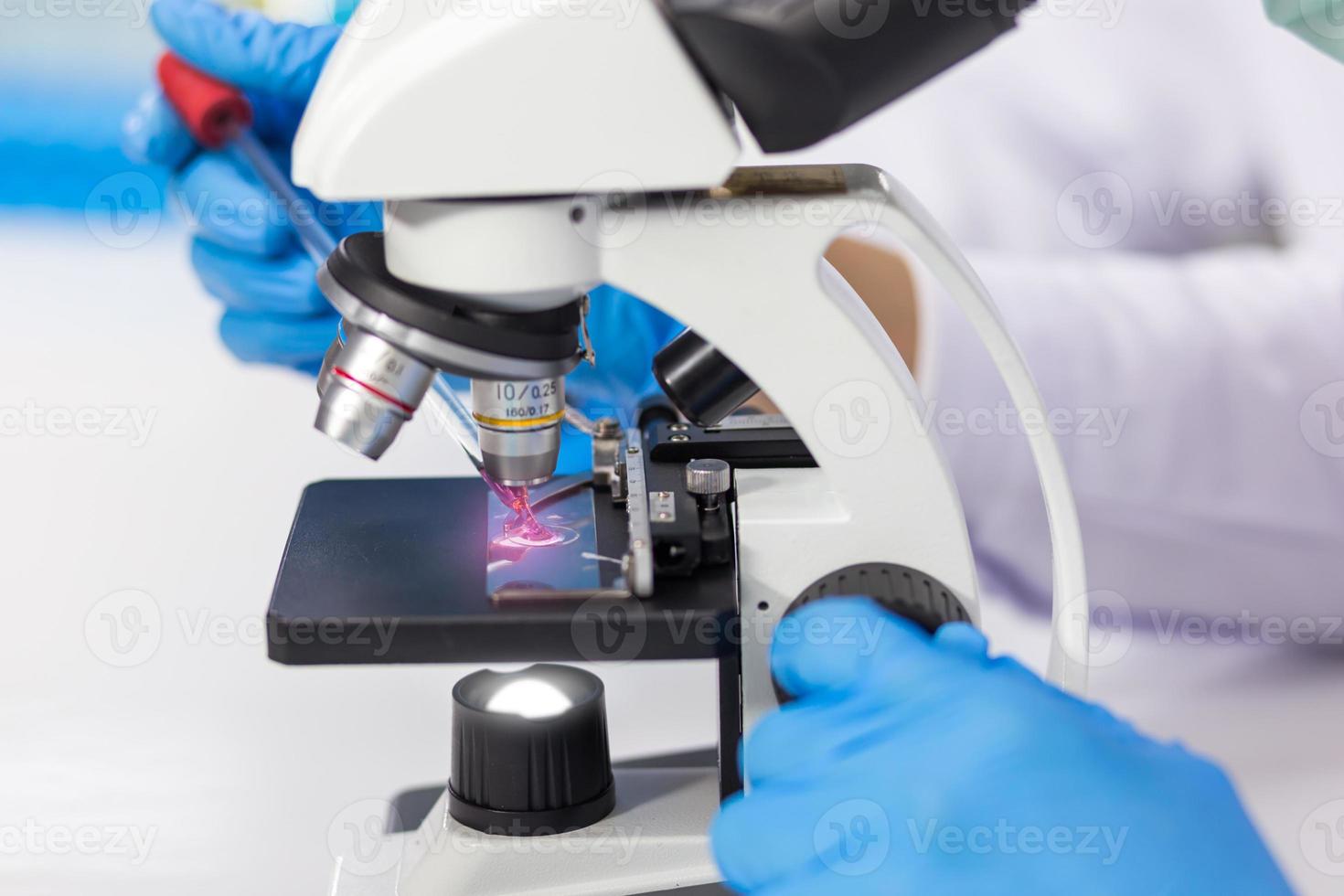 les mains d'hommes portant des gants en caoutchouc bleu utilisent un microscope pour travailler en laboratoire. photo
