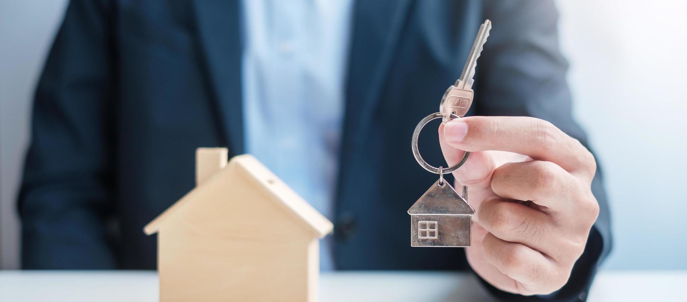 main d'homme d'affaires tenant la clé avec le modèle de maison en bois. immobilier, achat et vente, assurance des biens, concepts de contrat de location et de contrat photo