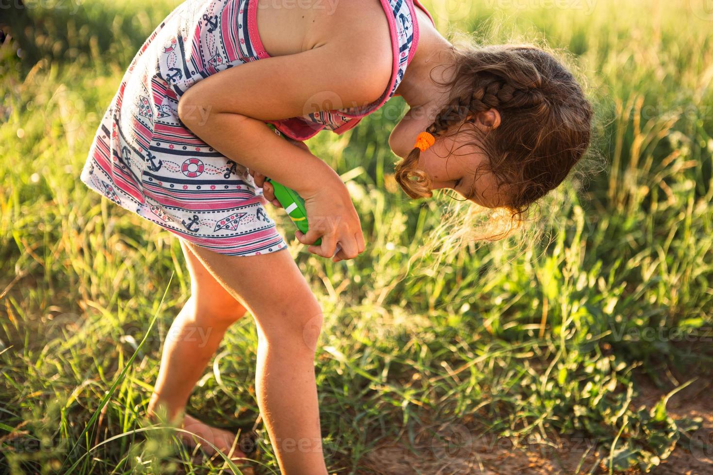 fille pulvérise un spray anti-moustique sur la peau dans la nature qui lui mord les mains et les pieds. protection contre les piqûres d'insectes, répulsif sans danger pour les enfants. loisirs de plein air, contre les allergies. heure d'été photo