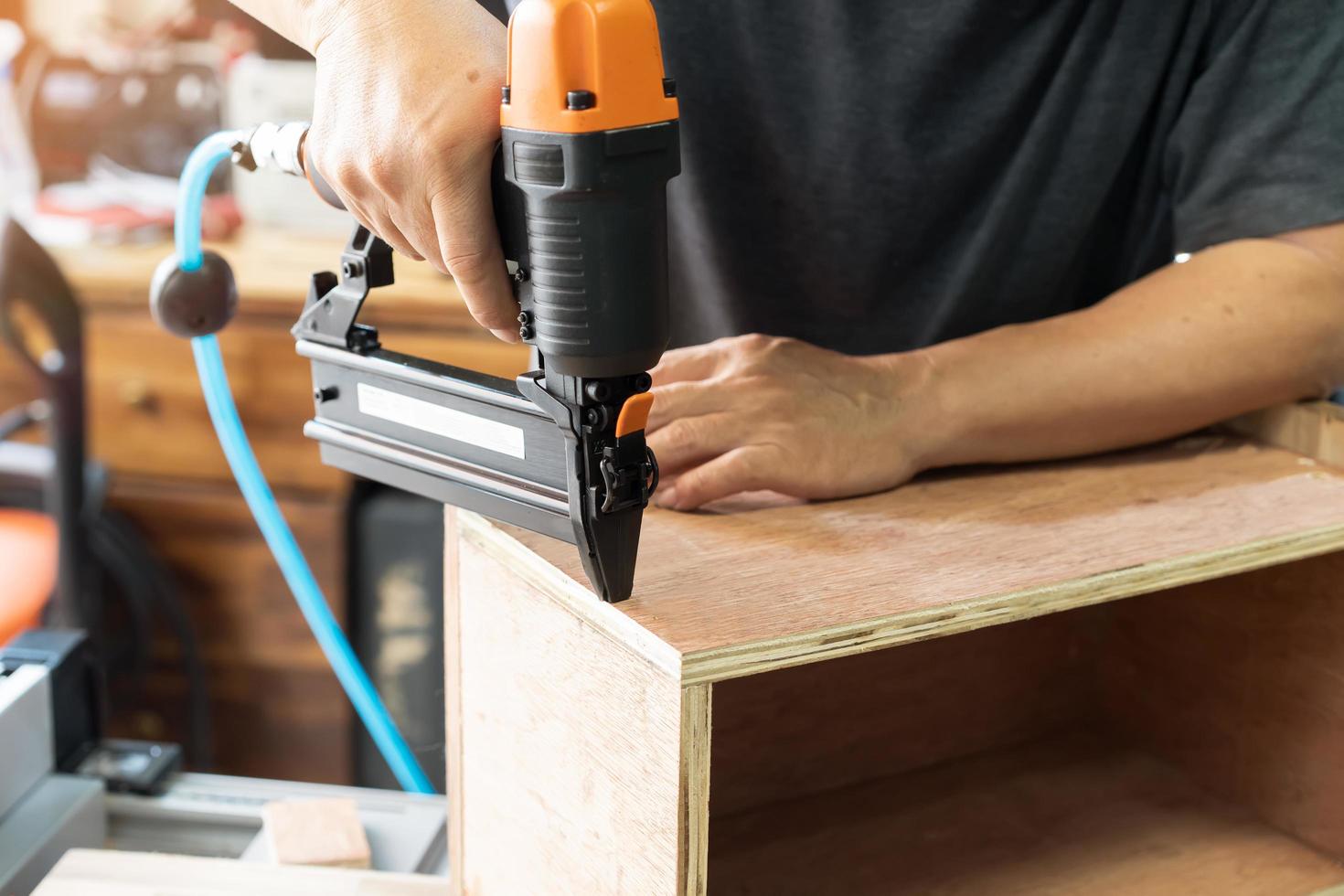charpentier à l'aide d'un pistolet à clous ou d'un outil de clouage brad sur une boîte en bois dans un atelier, concept de menuiserie de restauration de meubles. mise au point sélective photo