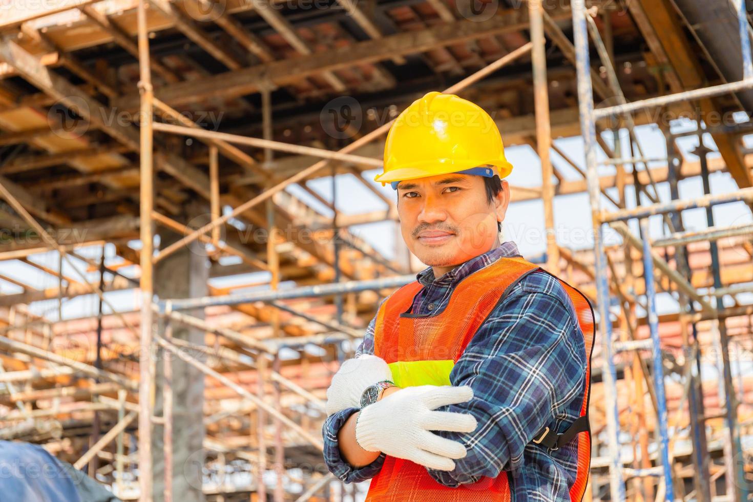 ingénieur homme ouvrier vérifiant et planifiant le projet sur le chantier de construction, homme souriant avec les bras croisés sur fond flou photo