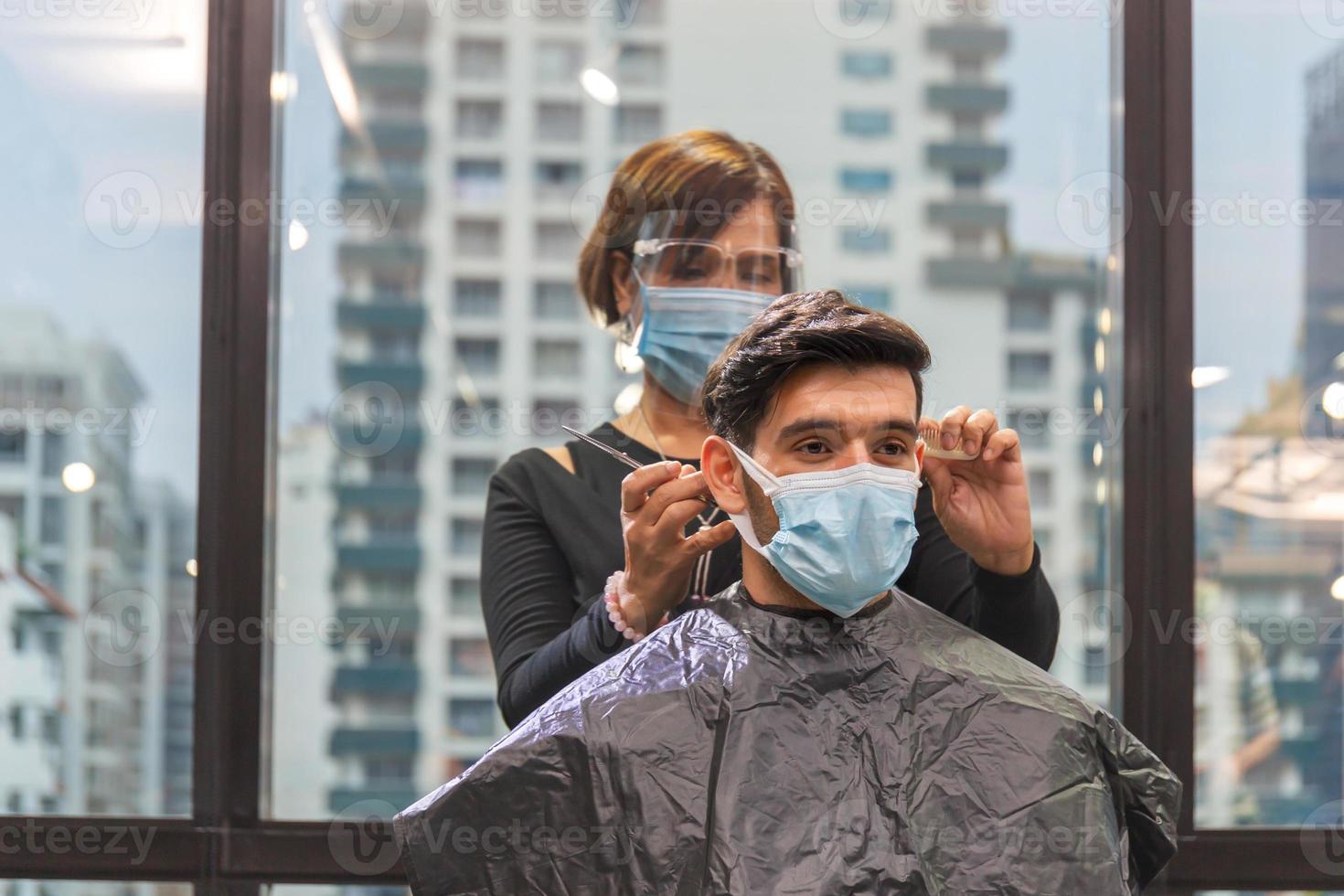 jeune homme se faisant couper les cheveux par un coiffeur, coiffeur utilisant des ciseaux et un peigne, nouveaux concepts normaux photo