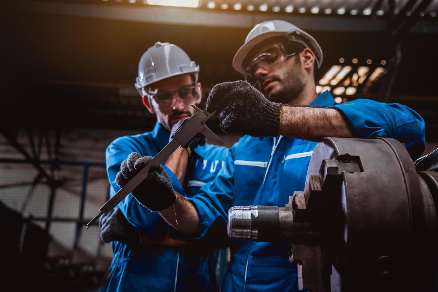 ingénierie de l'industrie portant un contrôle uniforme de sécurité faisant fonctionner une machine de meulage de tour contrôlée par ordinateur travaillant dans l'usine de l'industrie. photo