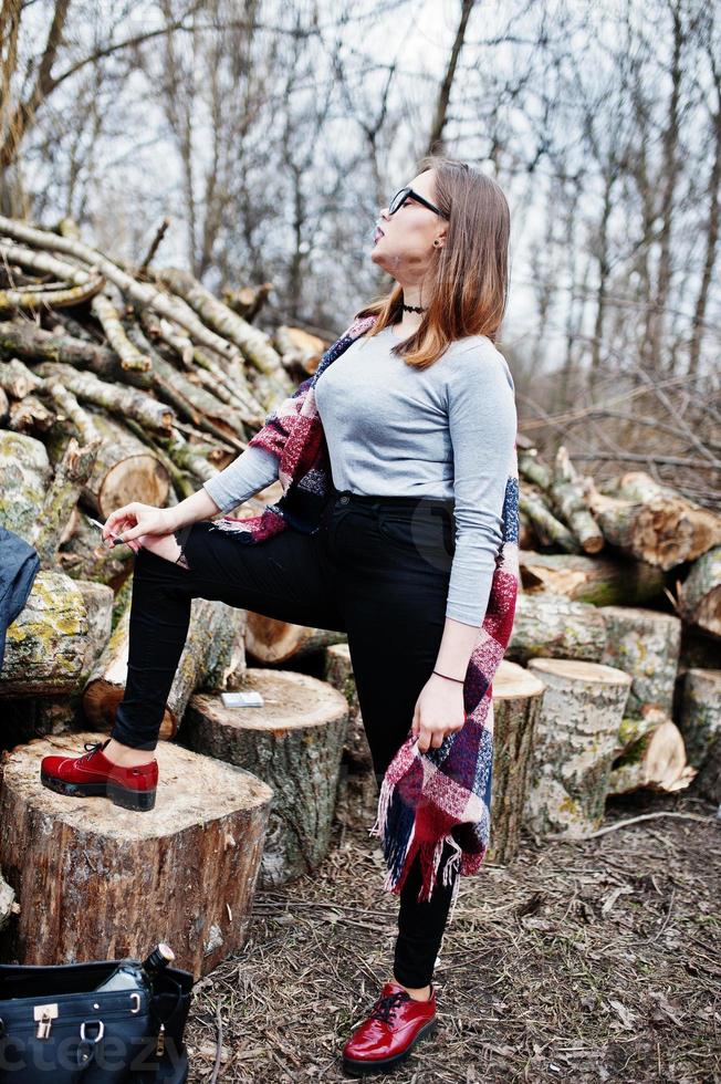 jeune fille ivre fumant une cigarette à l'extérieur des souches en bois de fond. concept de dépendance à la nicotine et à l'alcool chez les adolescents. photo