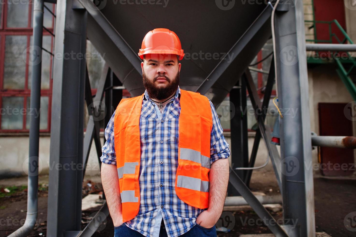 travailleur de la barbe brutal homme costume ouvrier du bâtiment en sécurité casque orange rester près du grand baril industriel . photo