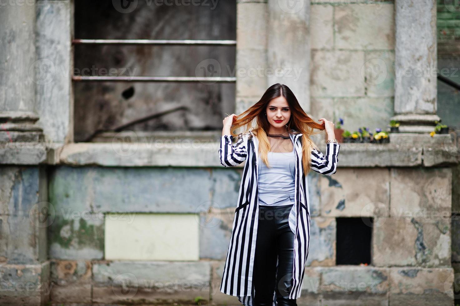 look femme à la mode avec une veste de costume à rayures noires et blanches, un pantalon en cuir, posant dans la vieille rue. concept de fille de mode. photo