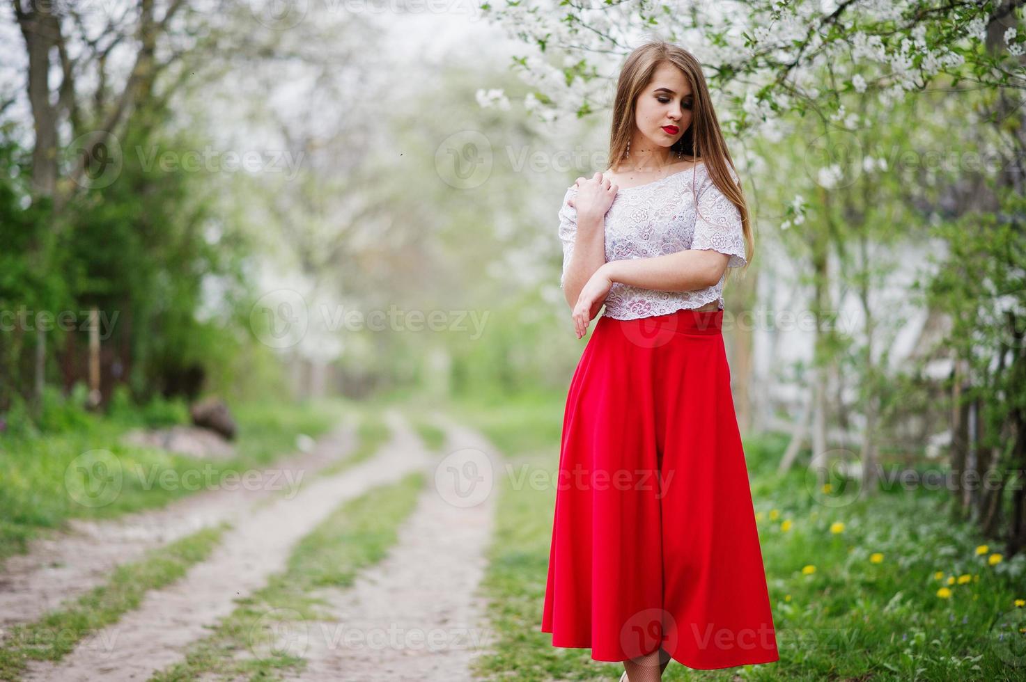 portrait de belle fille aux lèvres rouges au jardin de fleurs de printemps, porter une robe rouge et un chemisier blanc. photo