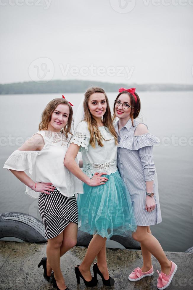 mariée fantastique avec ses deux demoiselles d'honneur sur le quai au bord du lac à l'enterrement de vie de jeune fille. photo