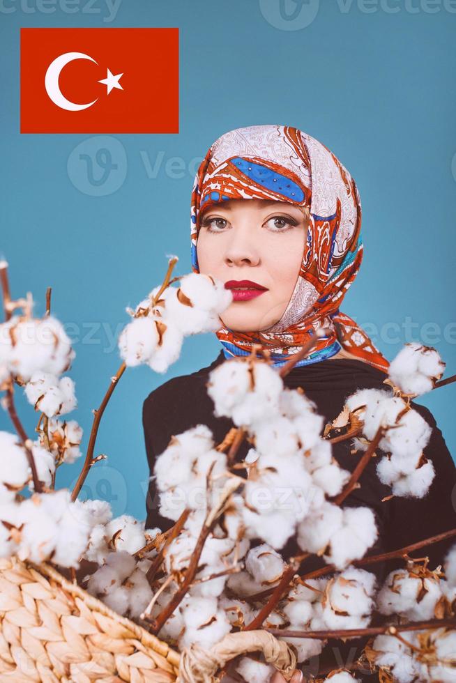orient femme dans un mouchoir coloré tenant un panier avec des branches de coton sur fond bleu. cueilleur de coton photo