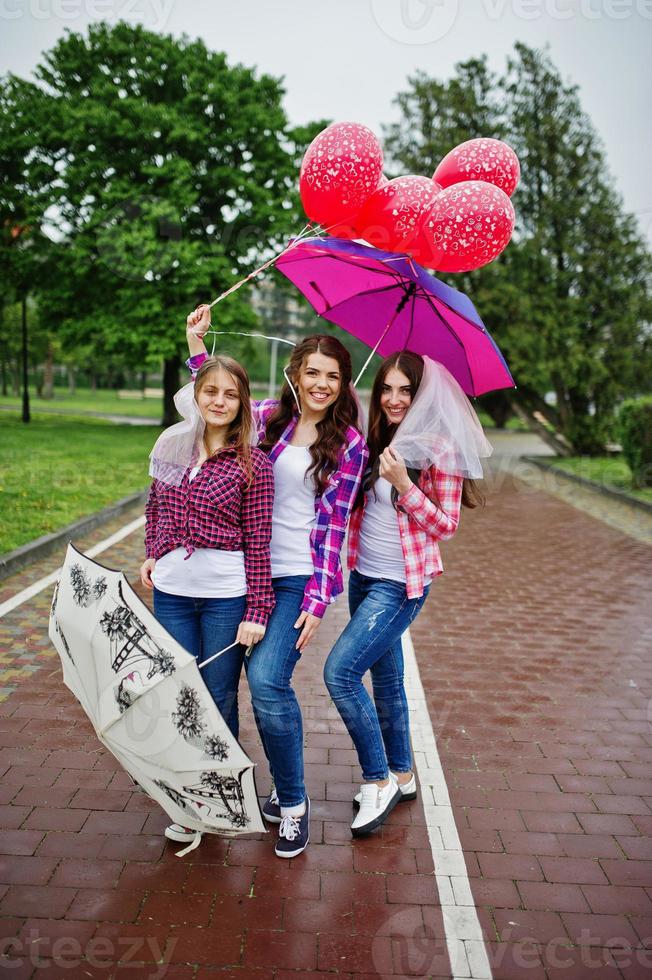 groupe de trois filles s'amusant à la fête de poule, avec parapluie sous la pluie et ballons. photo