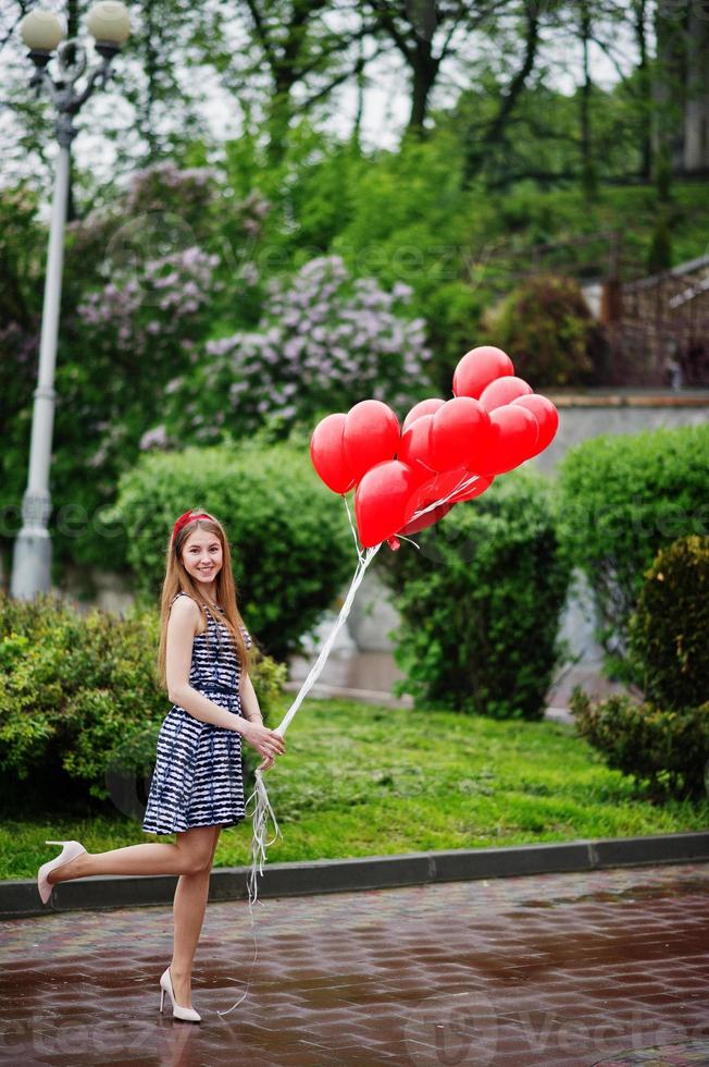 portrait d'une magnifique belle demoiselle d'honneur dans une jolie robe tenant des ballons rouges en forme de coeur dans le parc lors d'une soirée entre célibataires. photo