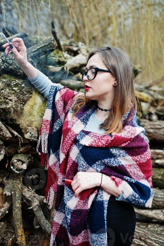 jeune fille fumant une cigarette à l'extérieur des souches en bois de fond. concept de dépendance à la nicotine chez les adolescents. photo