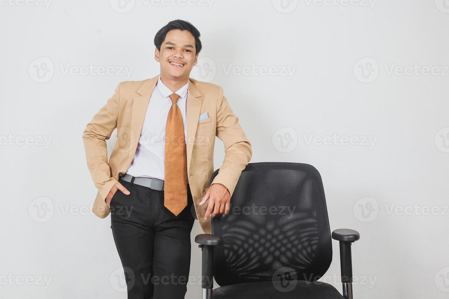 Un homme d'affaires asiatique à l'air intelligent s'appuie sur une chaise de bureau vide photo
