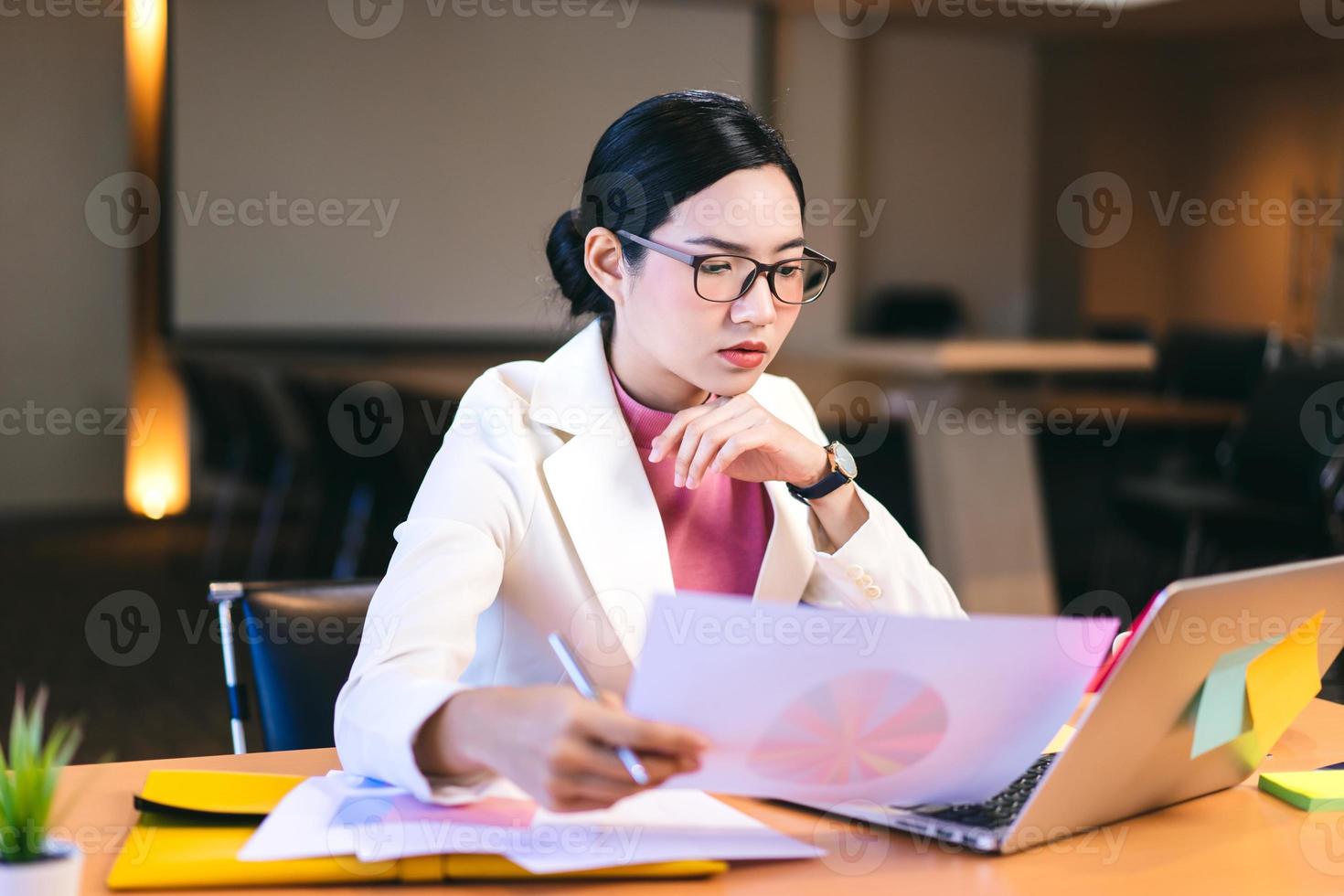 une femme asiatique travaillant dans une entreprise avec des lunettes lit un document à partir d'un ordinateur. photo