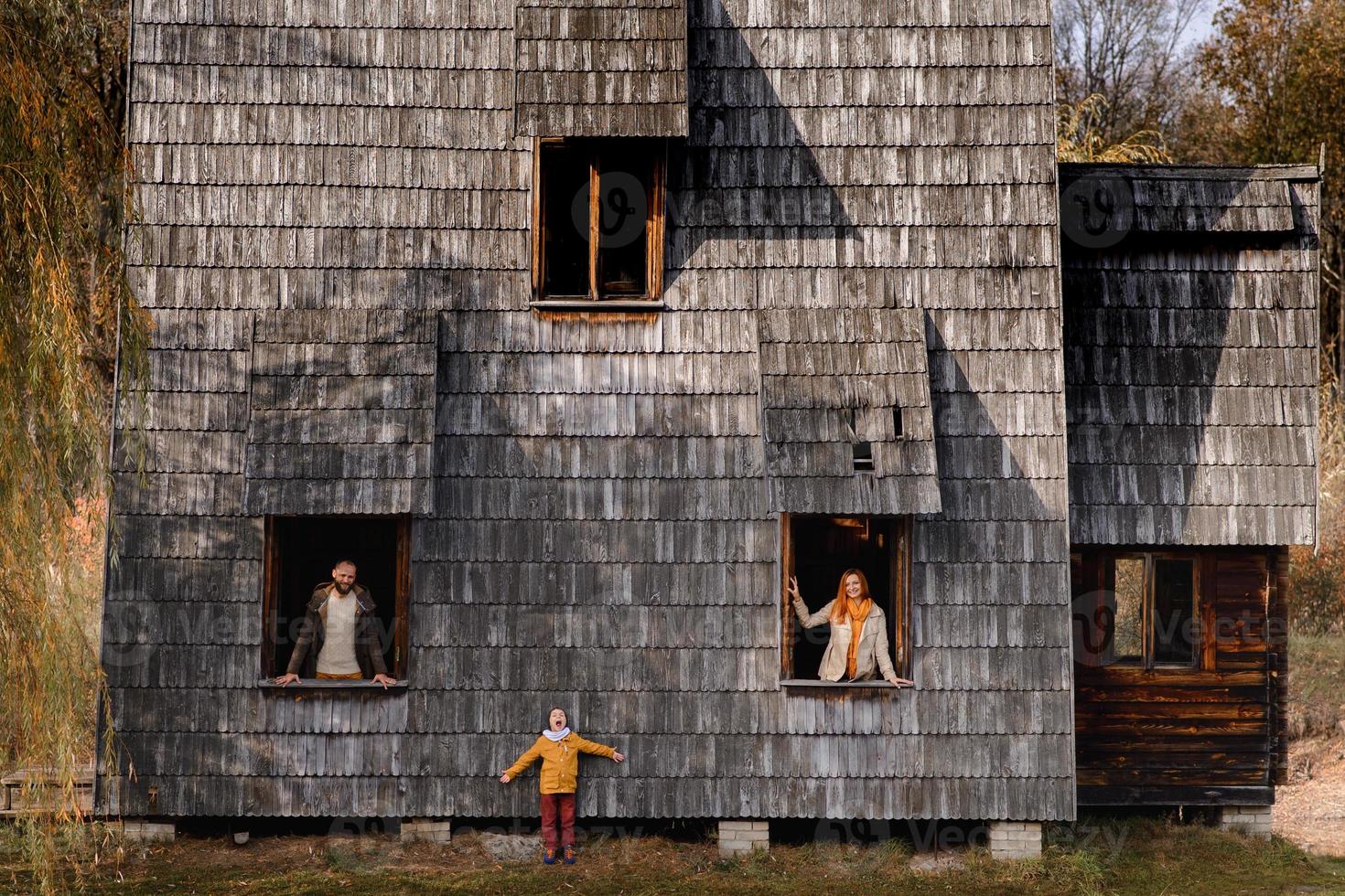 heureuse jeune famille regardant par les fenêtres d'une grande maison en bois. le concept d'acheter une maison, de louer une maison, pour une famille photo