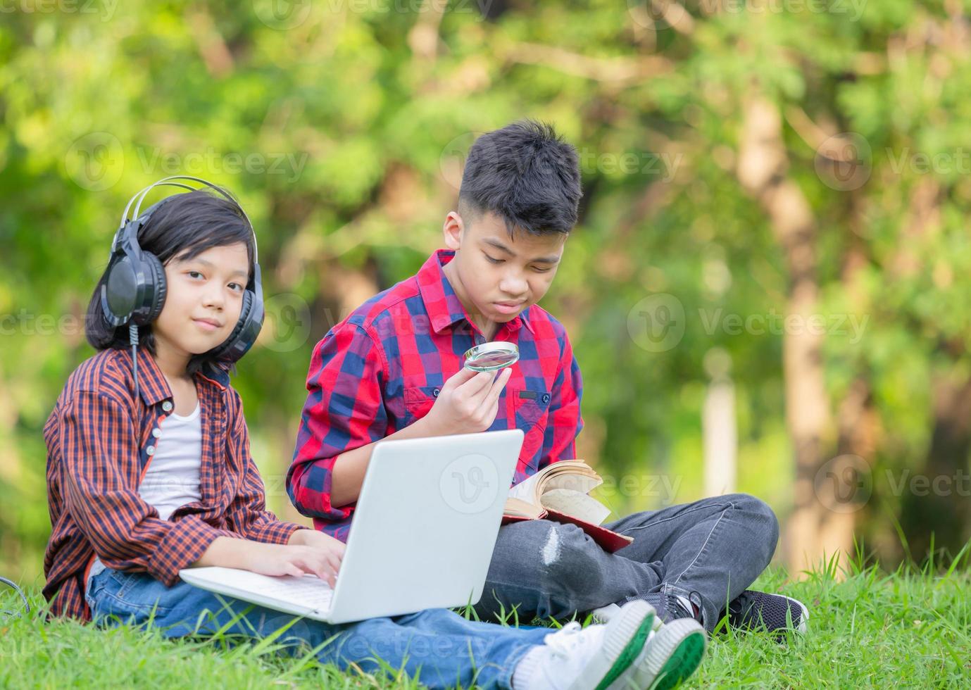 frère et soeur assis sur l'herbe avec un ordinateur portable, garçon et fille lisant le livre dans le parc, enfants jouant au concept d'apprentissage en plein air photo