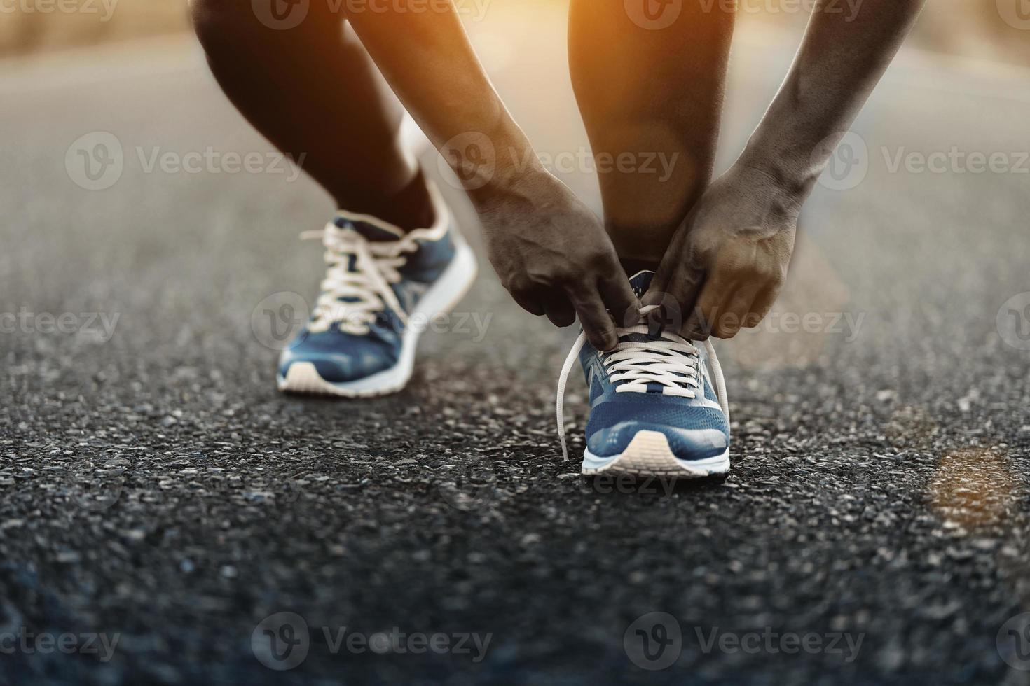 jeune coureur afro-américain attachant ses lacets sur la route en plein air. photo