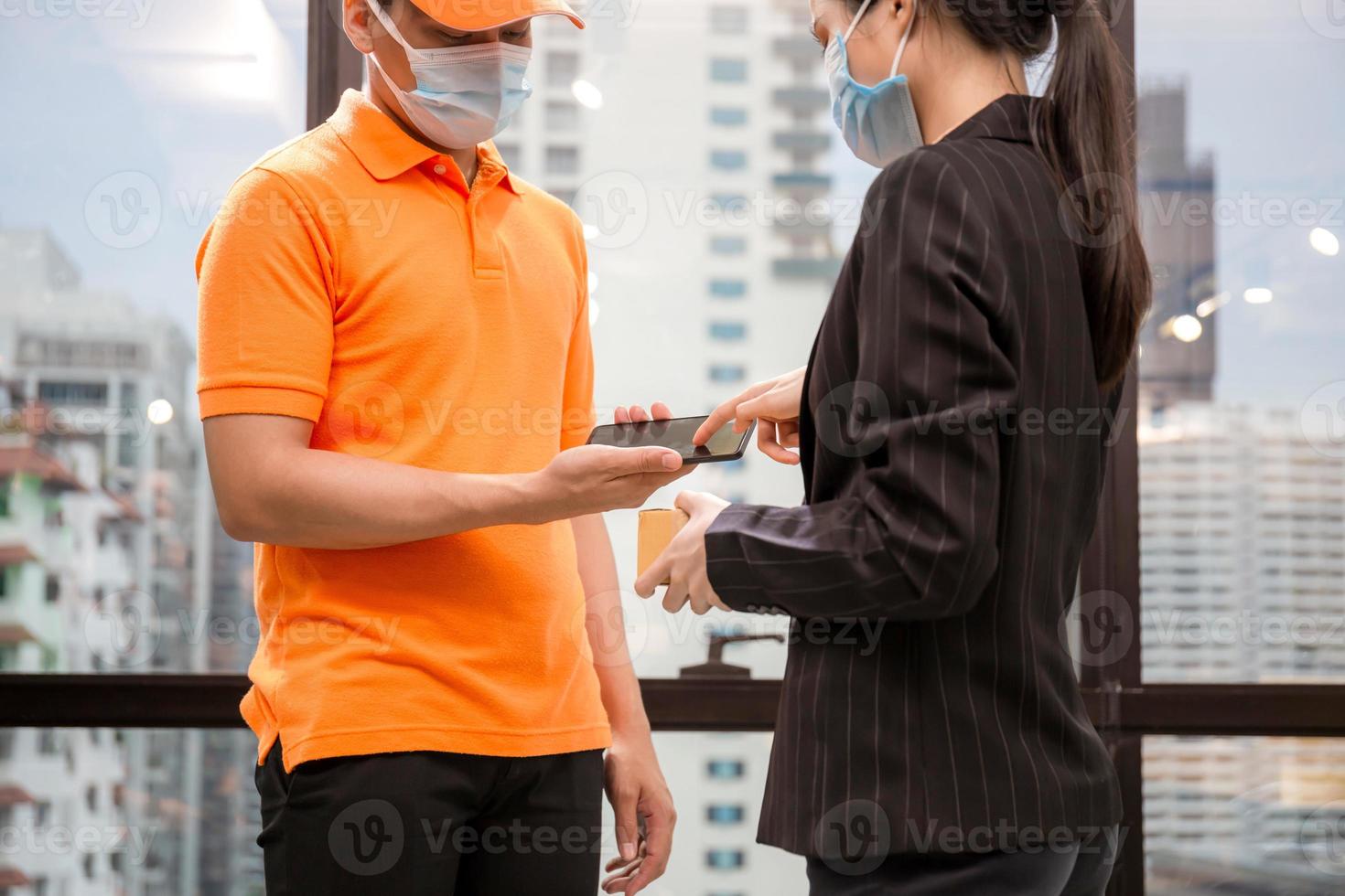 femme signant sur l'appareil pour livrer le colis, jeune livreur employé en uniforme de t-shirt portant un masque facial photo