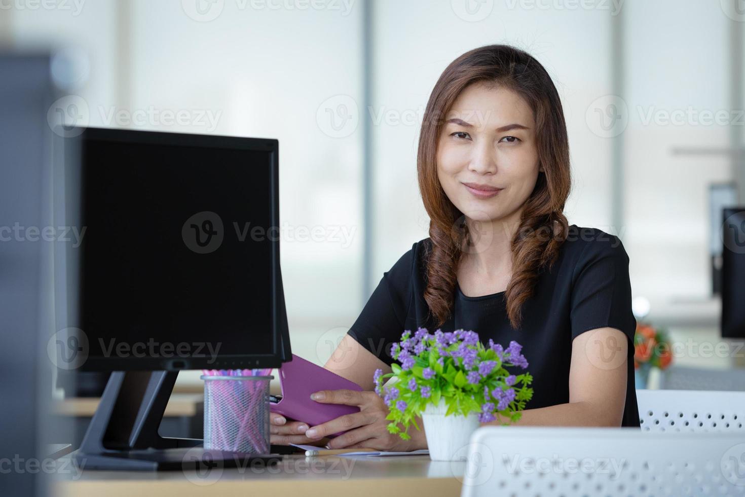 femme d'affaires asiatique senior assise au bureau près d'un écran d'ordinateur et regardant la caméra avec confiance en soi photo