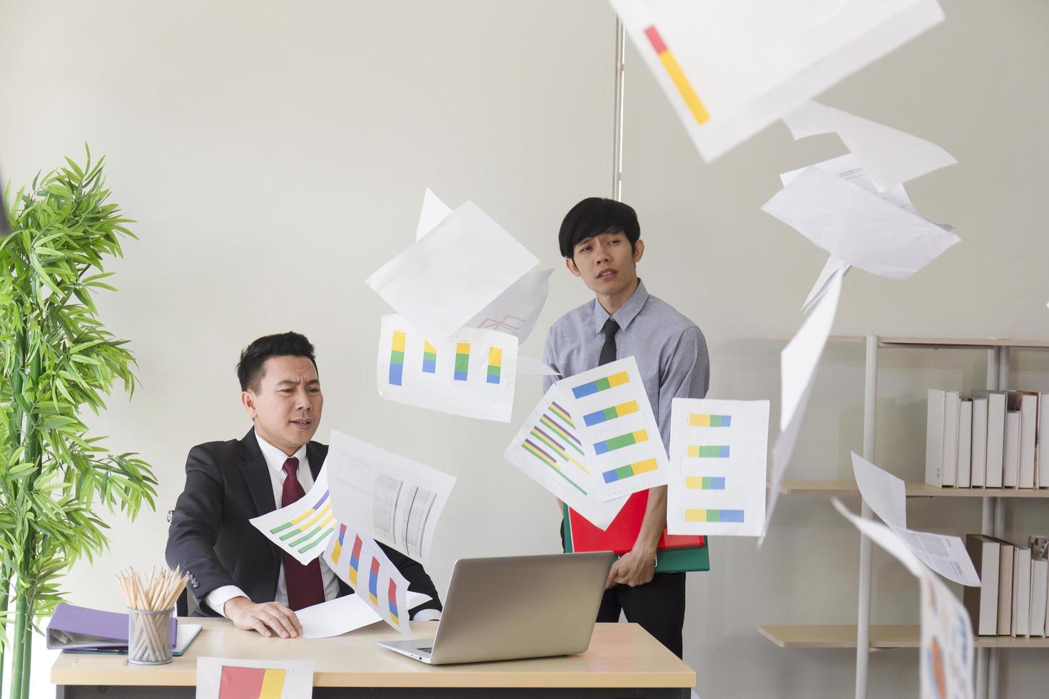 un manager asiatique en colère, ses employés incapables de travailler comme prévu, jetant du papier dans le bureau. photo