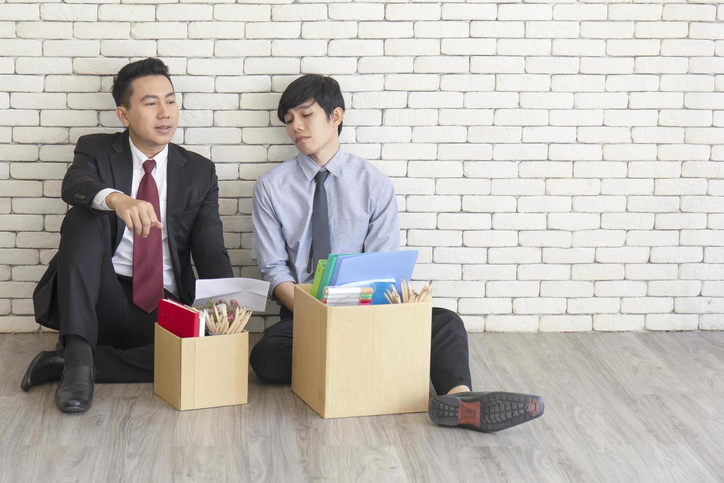 deux employés masculins étaient assis par terre et parlaient l'un devant l'autre avec une boîte en carton à usage personnel après avoir été licenciés du travail. photo