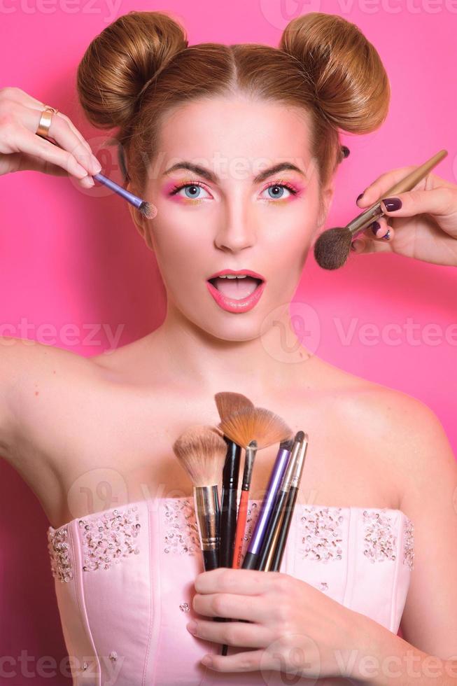 jolie femme blonde avec un maquillage coloré avec des pinceaux cosmétiques et des ombres en elle et maquille les mains du maître photo