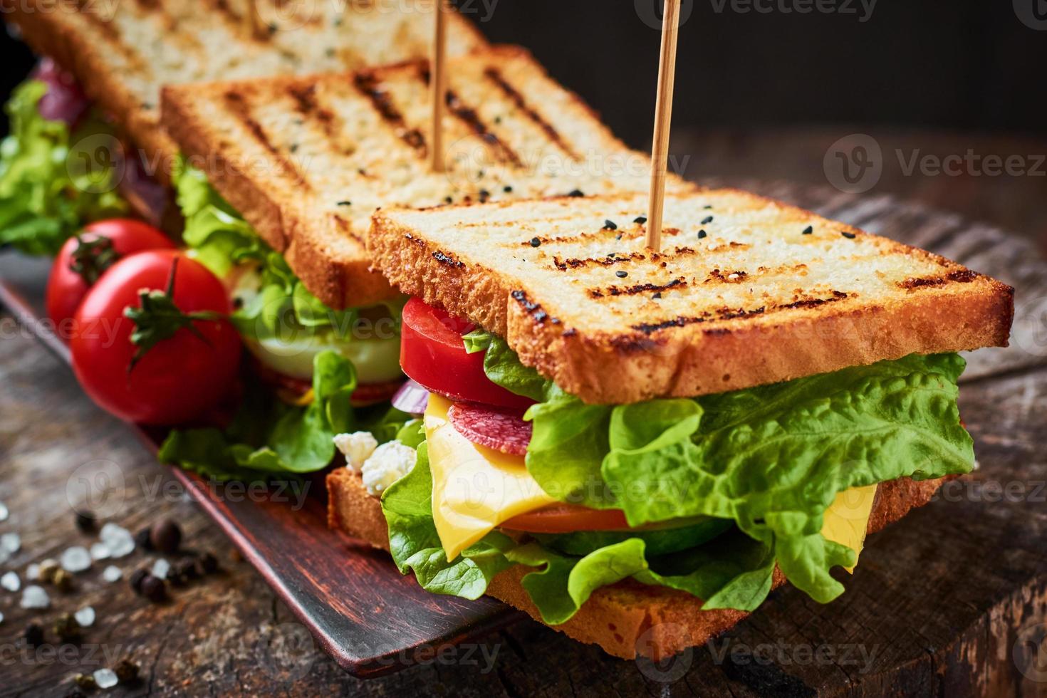 sandwich fait maison avec du jambon, de la laitue, du fromage et de la tomate sur un fond en bois photo