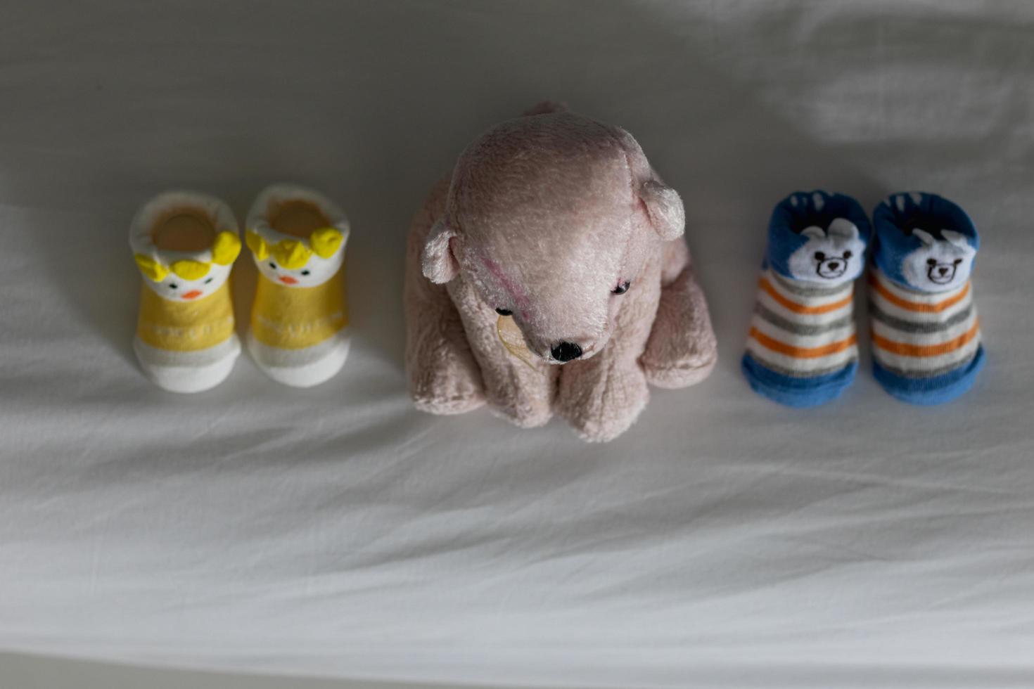 l'ours en peluche rose à poil court est assis près des chaussures du nouveau-né sur un matelas blanc dans la chambre qui prépare le bébé à la naissance. les femmes enceintes préparent des fournitures pour nouveau-nés et des jouets en peluche pour leurs bébés. photo