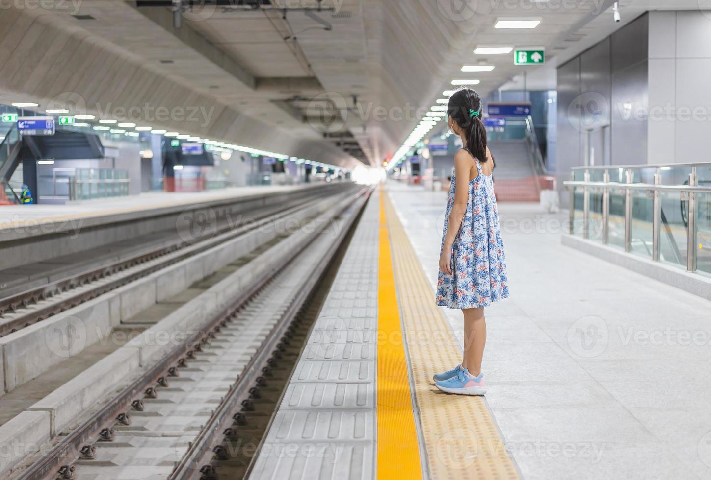 fille sur une gare, attendant le train, enfant attendant sur la plate-forme du tube, voyageant en chemin de fer. photo