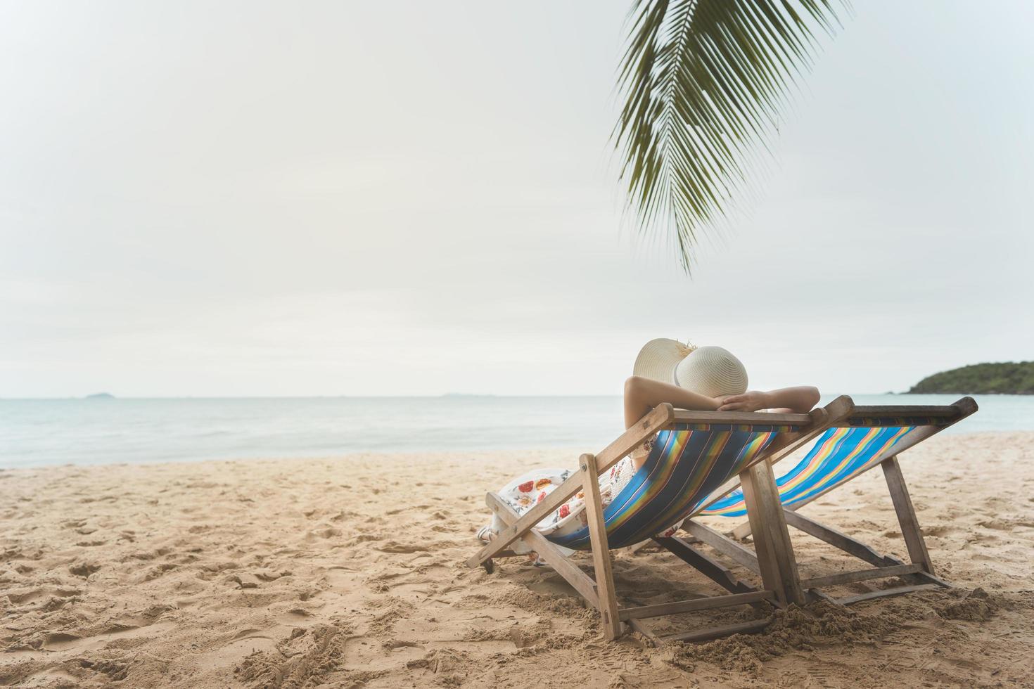 jeune femme asiatique se reposant sur une chaise de plage bras levé la main avec un chapeau souple photo