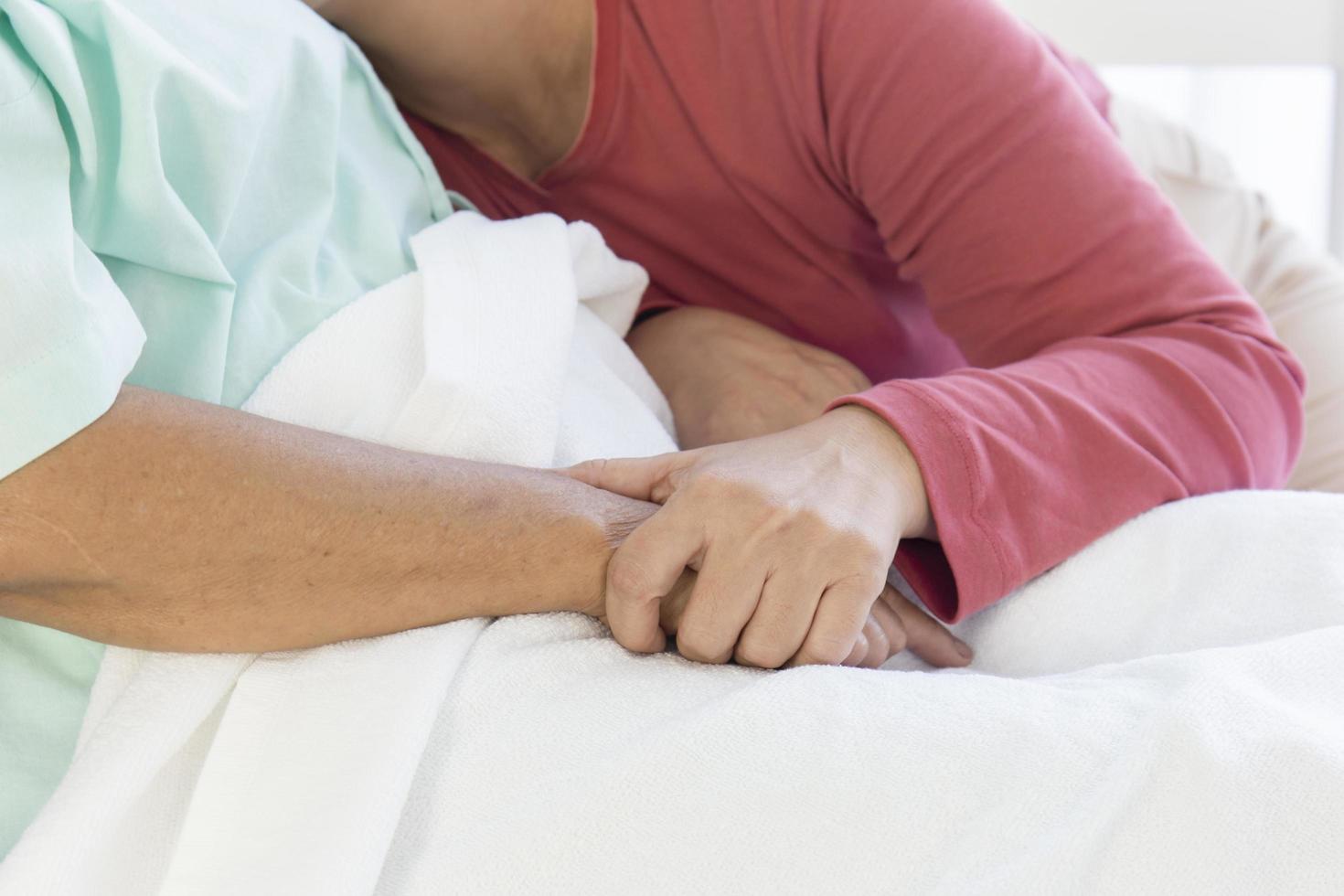 main dans la main avec une mère âgée malade allongée dans un lit d'hôpital avec chaleur et soin photo