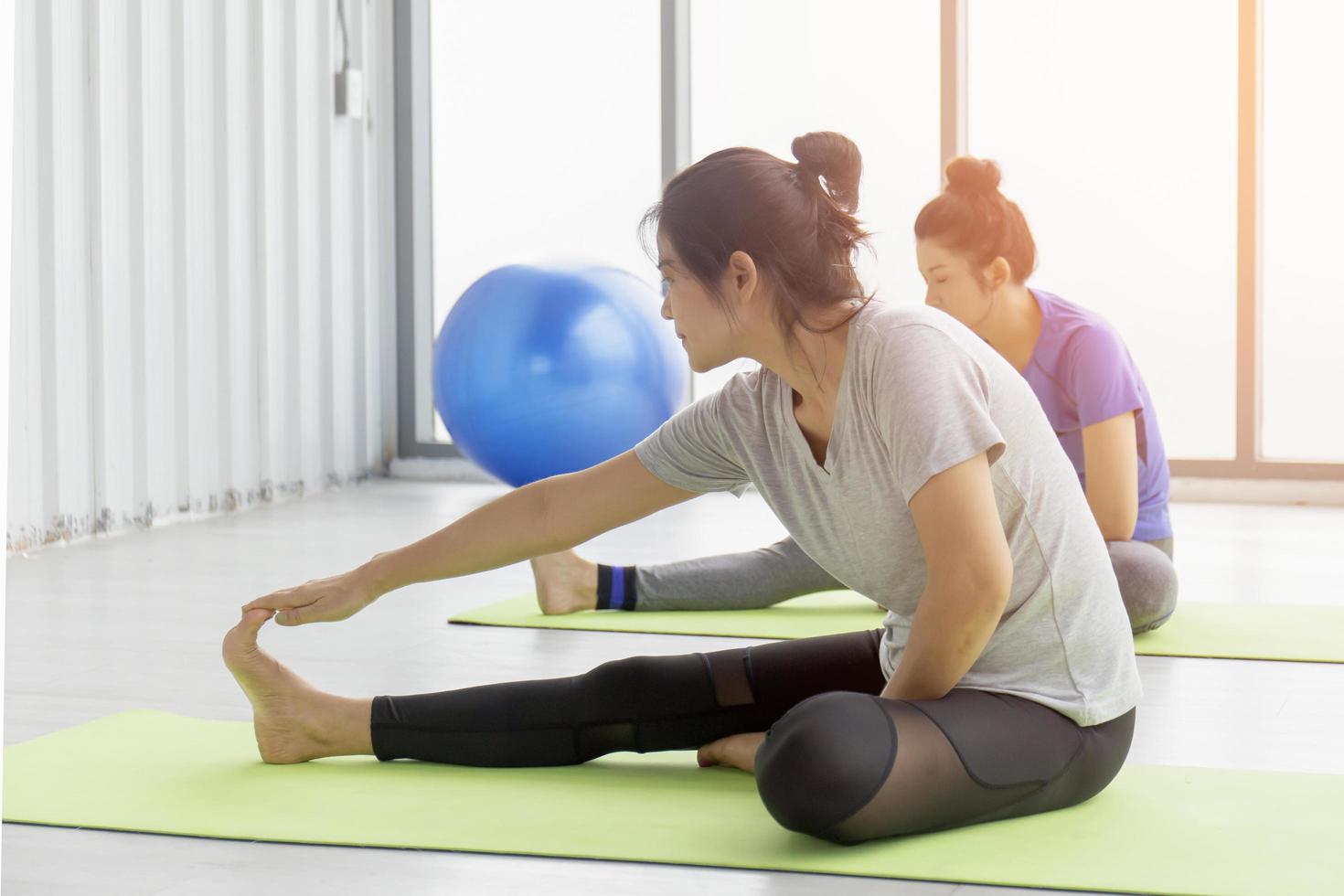 deux femmes asiatiques d'âge moyen faisant du yoga assises sur un tapis en caoutchouc dans une salle de sport. photo