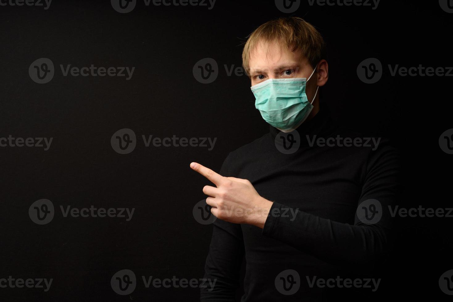 un homme en vêtements noirs sur fond noir dans un masque de protection vend votre produit. photo