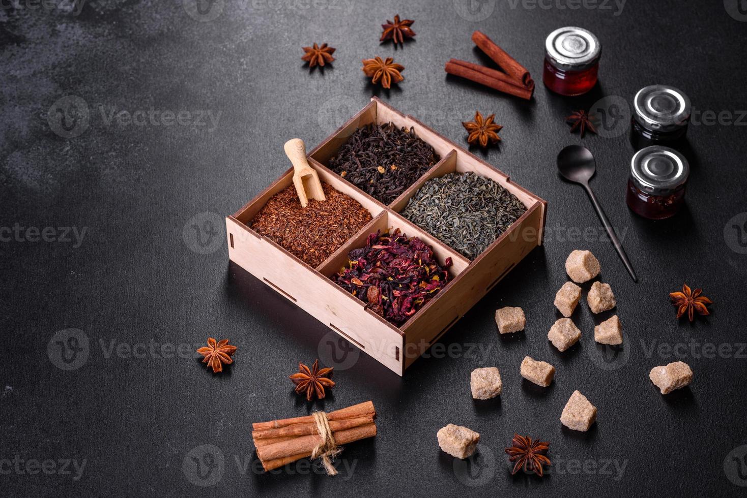 plusieurs sortes de thé noir sec à la bergamote, rooibos, vert et cadre dans une boîte en bois sur fond de béton noir photo