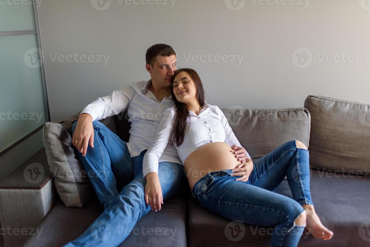 un homme et une femme enceinte sont assis enlacés sur le canapé. photo